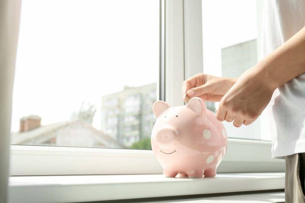 Woman Putting Money In A Piggy Bank By The Window